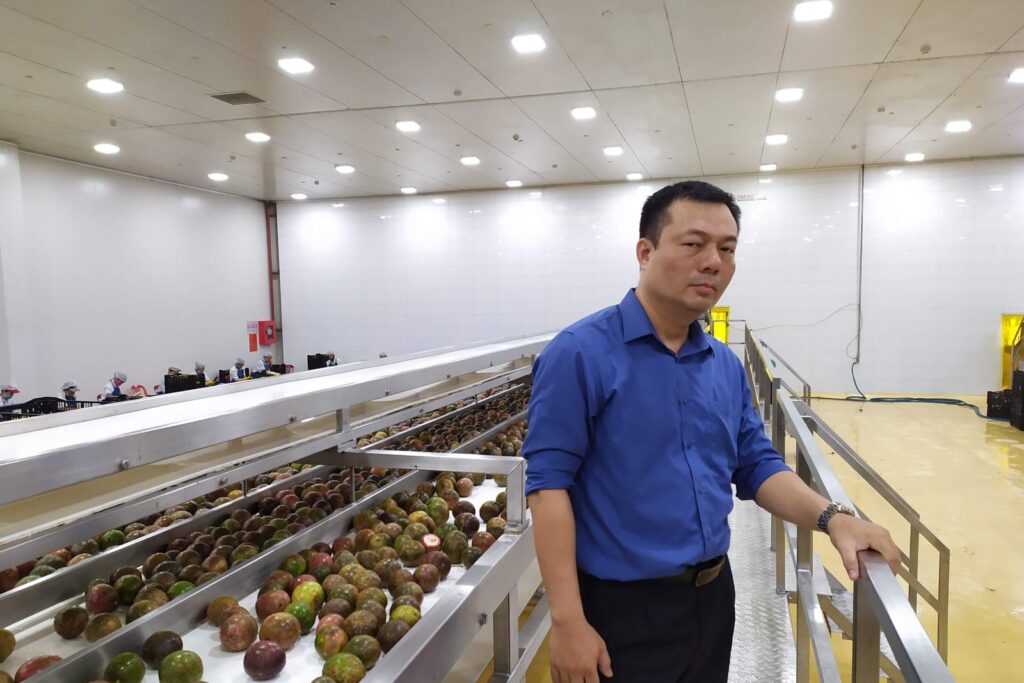 Paul Nguyen bên băng tải chanh dây trong nhà máy chế biến trái cây